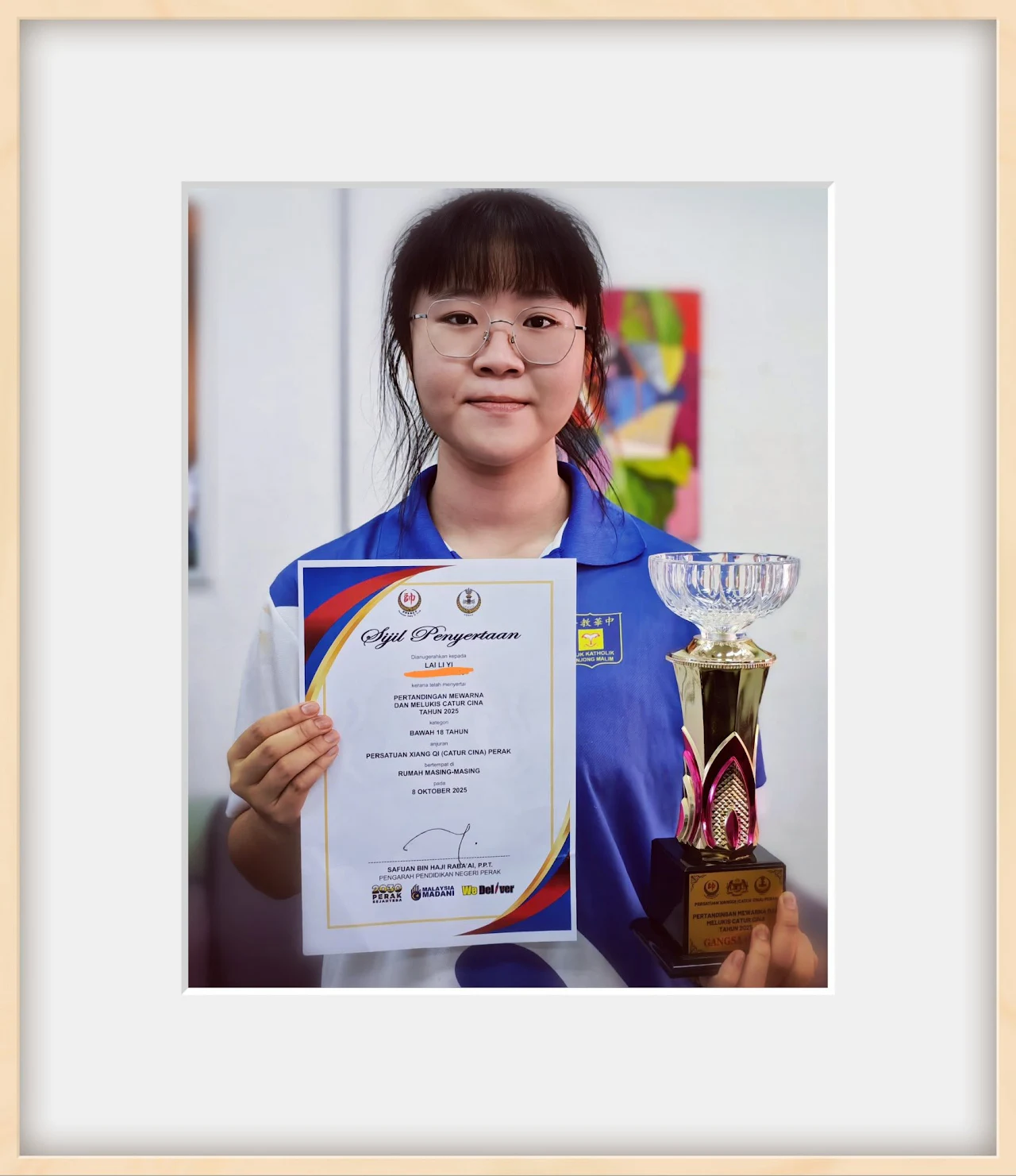 Student holding a certificate beside an achievement trophy