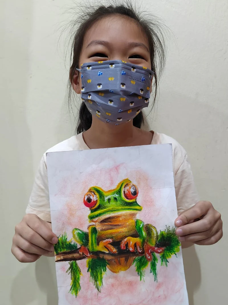 Student holding a colourful tree frog drawing