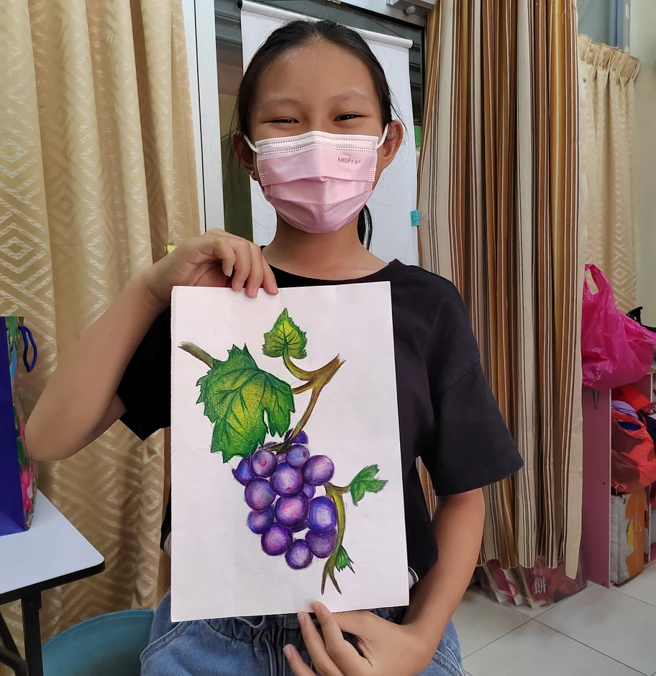 Student holding a coloured-pencil study of grapes and leaves
